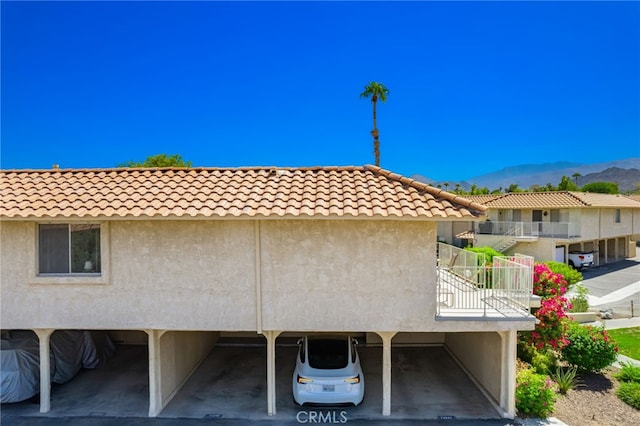 exterior space with a mountain view, stucco siding, covered parking, and a tile roof
