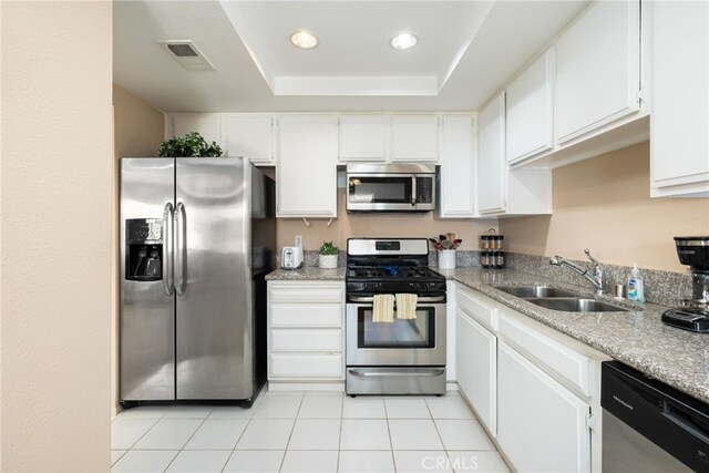 kitchen with stainless steel appliances, a sink, a tray ceiling, white cabinetry, and light tile patterned flooring