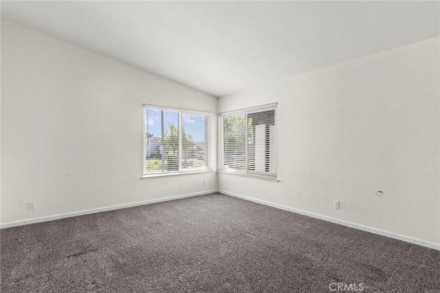 empty room featuring lofted ceiling, dark carpet, and baseboards