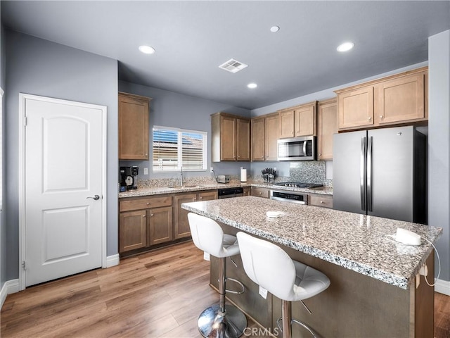 10630 Appaloosa Ave, Hesperia, CA 92345 - kitchen with appliances with stainless steel finishes, a sink, light wood-style floors, a kitchen island, and a breakfast bar