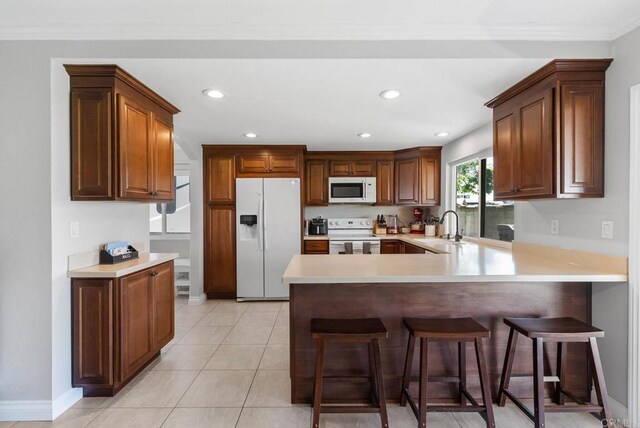 kitchen featuring white appliances, a sink, a peninsula, light countertops, and a breakfast bar