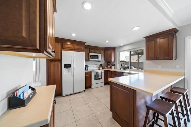kitchen featuring white appliances, a peninsula, a kitchen breakfast bar, light countertops, and a sink