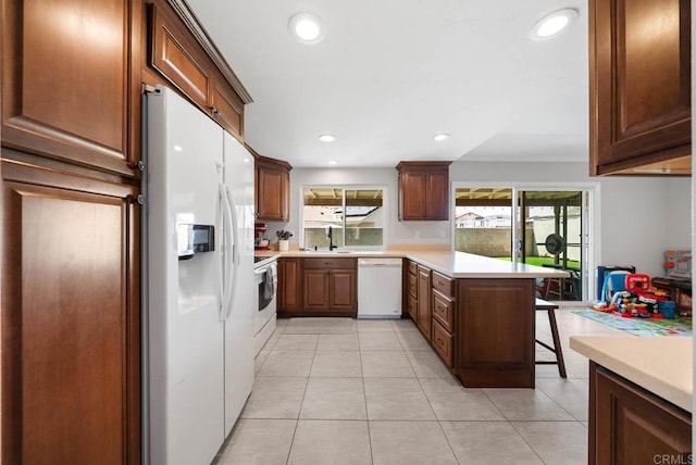 kitchen featuring white appliances, a peninsula, light countertops, a sink, and recessed lighting