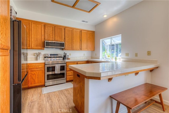 1918 Potter Rd, Chico, CA 95928 - kitchen featuring stainless steel appliances, a peninsula, brown cabinetry, light wood-style floors, and recessed lighting