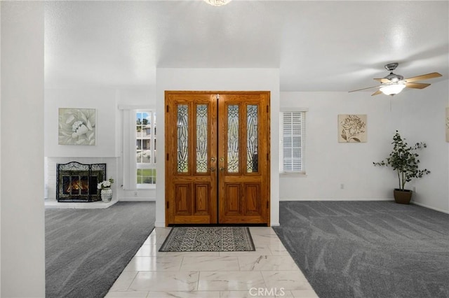 entrance foyer with light colored carpet, baseboards, a ceiling fan, and a brick fireplace
