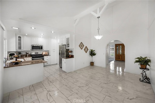 kitchen featuring stainless steel appliances, a sink, arched walkways, light marble finish floors, and white cabinets