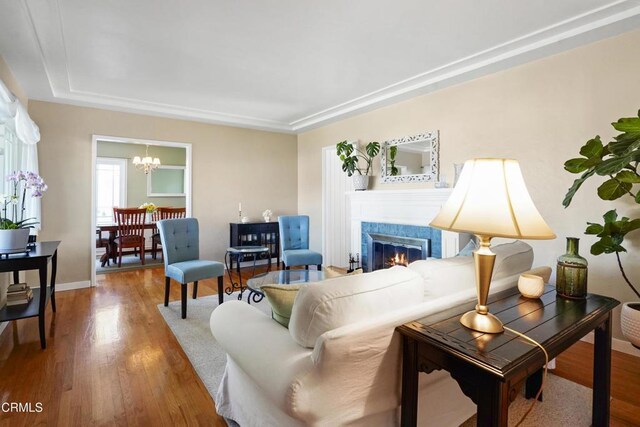 living room with wood finished floors, a tiled fireplace, a chandelier, and baseboards
