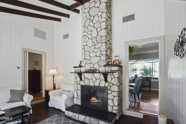 living room featuring wood finished floors, a stone fireplace, beamed ceiling, a towering ceiling, and wood walls