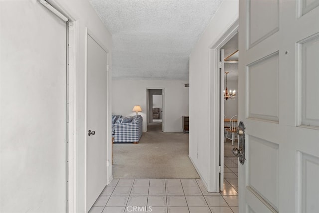 hallway featuring a textured ceiling, light tile patterned flooring, light colored carpet, and a chandelier