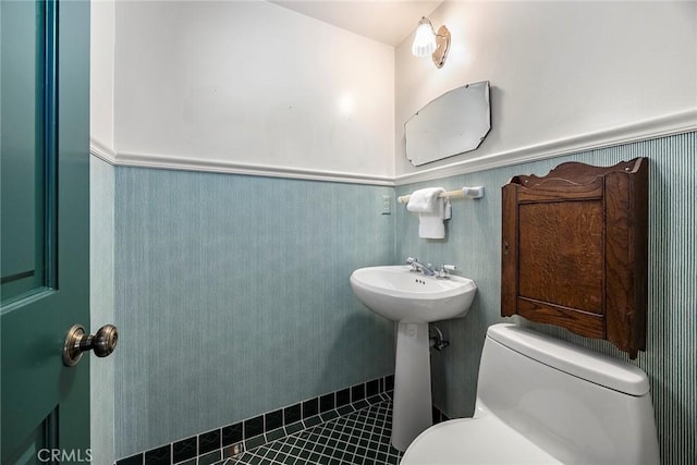 half bath with a wainscoted wall, toilet, and tile patterned flooring