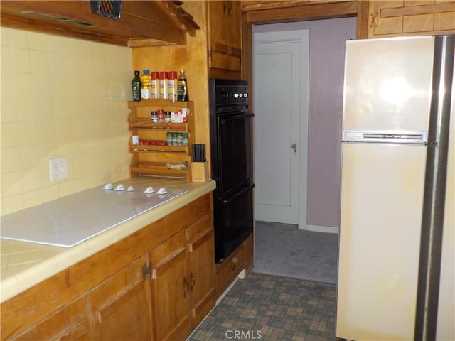 2698 Fremontia Dr, San Bernardino, CA 92404 - kitchen with freestanding refrigerator, tile counters, brown cabinets, dark colored carpet, and backsplash