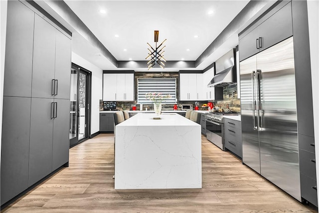 9218 Encino Ave, Northridge, CA 91325 - kitchen featuring premium appliances, a kitchen island, wall chimney exhaust hood, decorative backsplash, and light stone counters