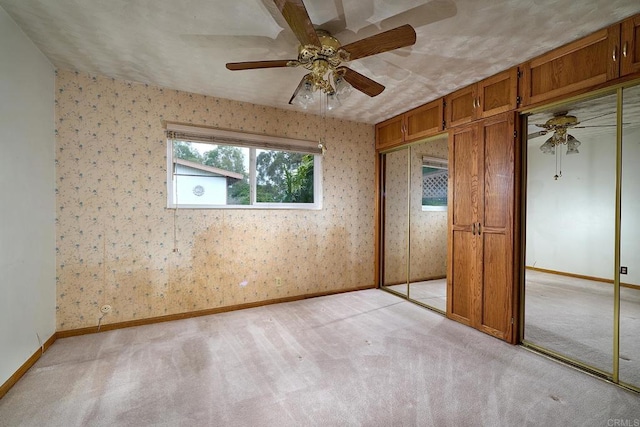 unfurnished bedroom with light colored carpet, baseboards, wallpapered walls, and a ceiling fan