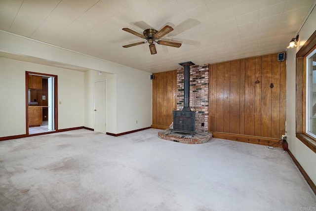 unfurnished living room featuring a wood stove, carpet floors, wood walls, and baseboards