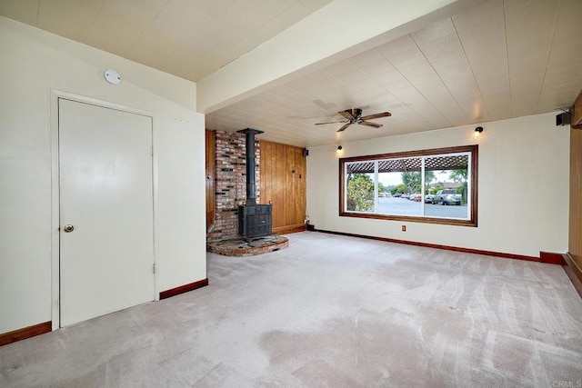 unfurnished living room with a wood stove, carpet, baseboards, and ceiling fan