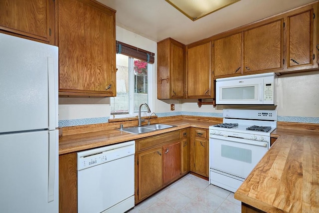 kitchen with white appliances, a sink, brown cabinetry, light tile patterned floors, and wood counters