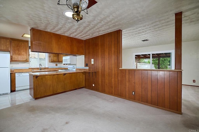 kitchen featuring white appliances, brown cabinetry, plenty of natural light, a sink, and wood walls