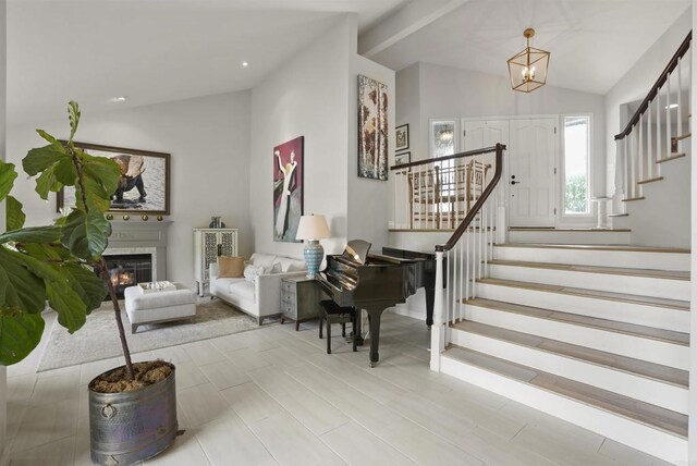 foyer featuring vaulted ceiling, stairway, a glass covered fireplace, a chandelier, and recessed lighting