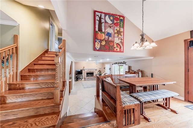 dining area featuring high vaulted ceiling, stairs, a chandelier, a fireplace, and crown molding