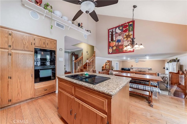 kitchen featuring black appliances, a ceiling fan, a towering ceiling, a center island, and light wood-style flooring