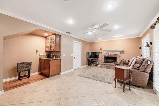 living area with a ceiling fan, crown molding, a brick fireplace, recessed lighting, and baseboards