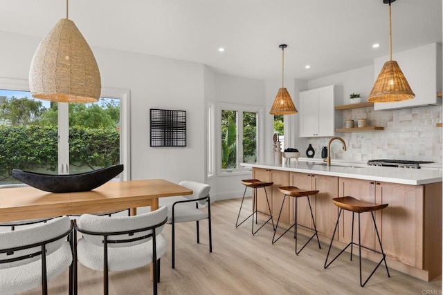 kitchen featuring a sink, tasteful backsplash, light countertops, recessed lighting, and light wood finished floors