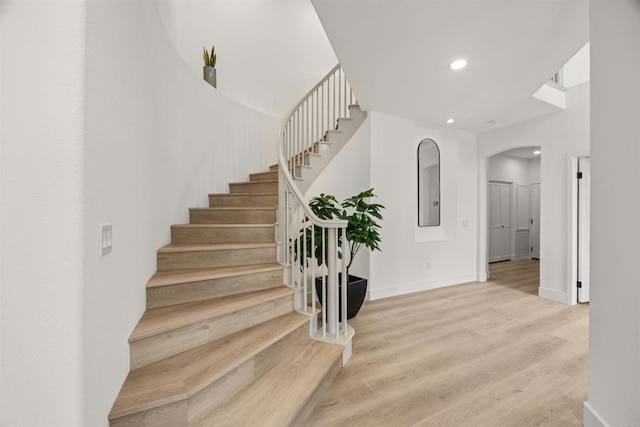stairway featuring arched walkways, recessed lighting, wood finished floors, and baseboards