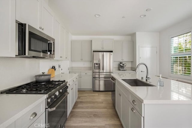 kitchen featuring appliances with stainless steel finishes, a sink, light countertops, light wood-style floors, and a kitchen island with sink