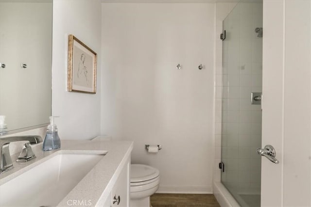 bathroom with toilet, a shower stall, baseboards, vanity, and wood finished floors