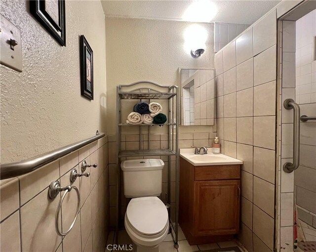 527 E King St, Rialto, CA 92376 - bathroom featuring tile walls, toilet, a textured wall, and vanity