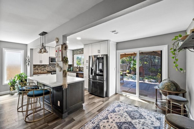 3221 Camarillo Ave, Oceanside, CA 92056 - kitchen with appliances with stainless steel finishes, decorative backsplash, a kitchen breakfast bar, white cabinetry, and decorative light fixtures