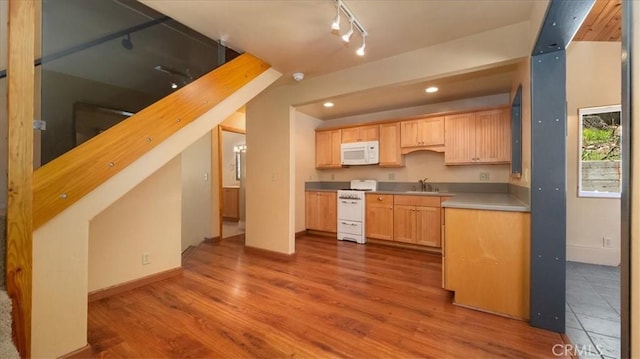 kitchen with white appliances, a sink, track lighting, light brown cabinets, and wood finished floors