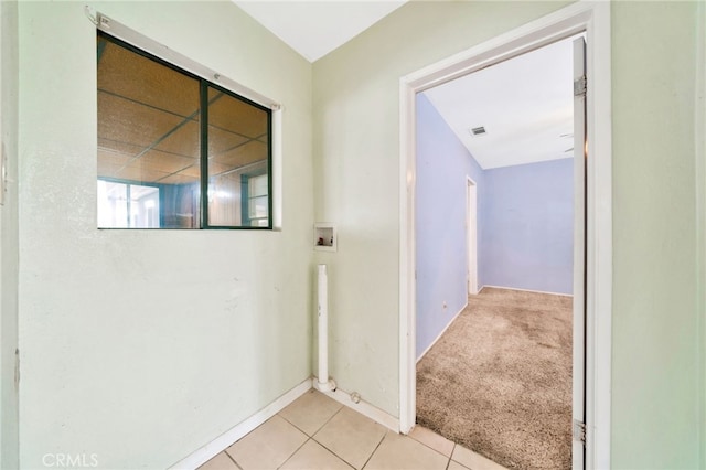 hallway with light tile patterned floors, baseboards, and light colored carpet