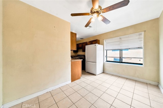 kitchen featuring freestanding refrigerator, baseboards, a ceiling fan, light tile patterned flooring, and gas range