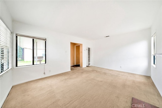 spare room featuring light colored carpet, healthy amount of natural light, and baseboards