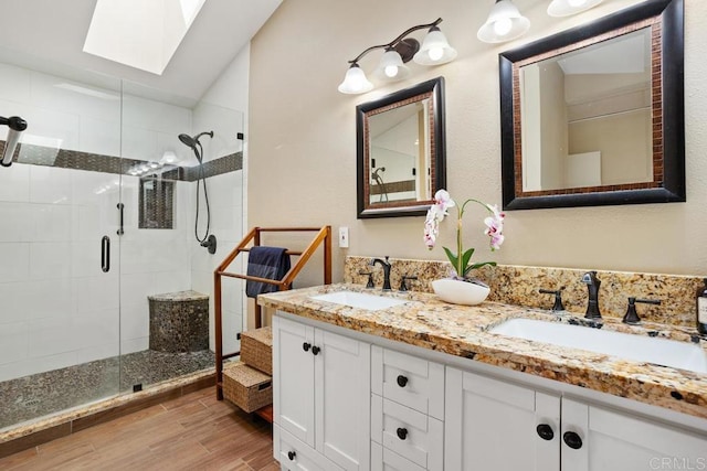 bathroom with a skylight, wood finished floors, a shower stall, double vanity, and vaulted ceiling