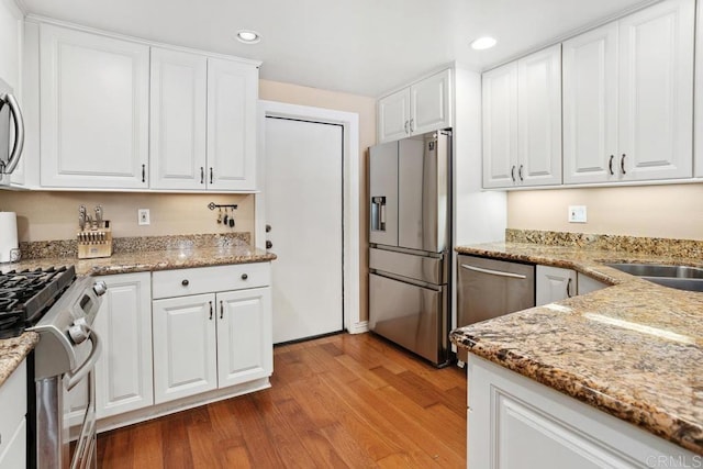 kitchen featuring appliances with stainless steel finishes, recessed lighting, wood finished floors, white cabinets, and light stone counters