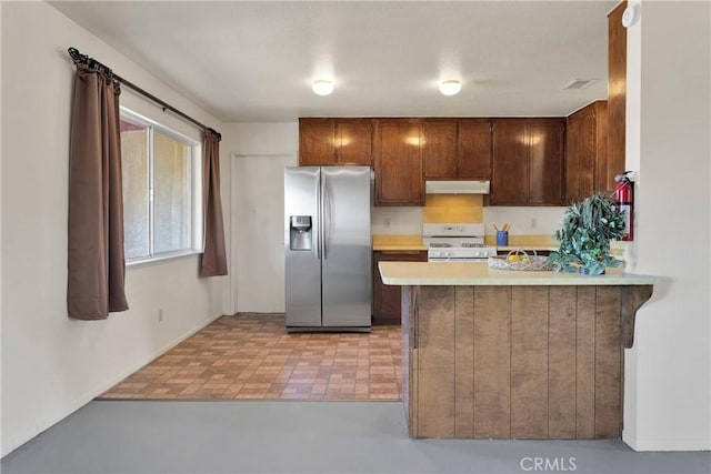 kitchen featuring stainless steel fridge with ice dispenser, white gas range oven, under cabinet range hood, light countertops, and a peninsula