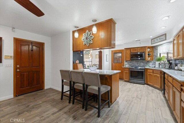 1995 E Valley Forge Ave, Tulare, CA 93274 - kitchen featuring stainless steel appliances, brown cabinetry, light wood-style flooring, decorative backsplash, and light countertops