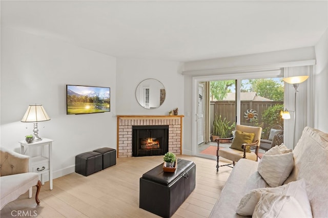 living room with light wood finished floors, a brick fireplace, and baseboards