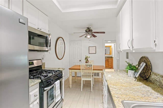 kitchen featuring appliances with stainless steel finishes, ceiling fan, white cabinets, light stone counters, and baseboards