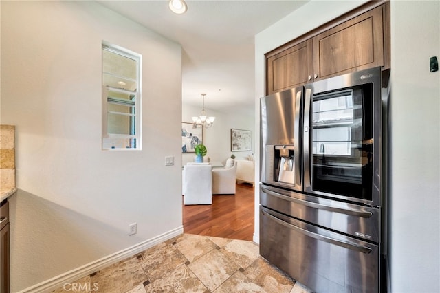 kitchen featuring stainless steel refrigerator with ice dispenser, a chandelier, baseboards, light stone finish flooring, and light countertops