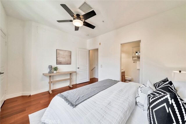 bedroom with wood finished floors, baseboards, ensuite bath, a ceiling fan, and attic access