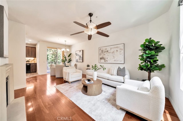 living area featuring a ceiling fan, light wood-type flooring, a chandelier, and baseboards