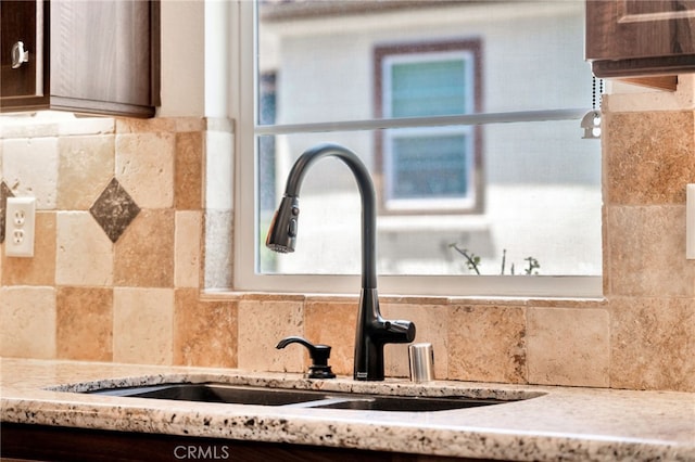 kitchen view of backsplash, a sink, and dark brown cabinetry