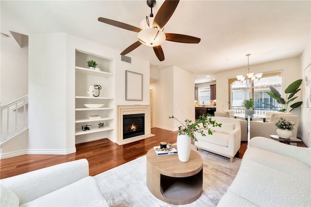 living room featuring built in features, light wood finished floors, baseboards, a ceiling fan, and a fireplace with flush hearth