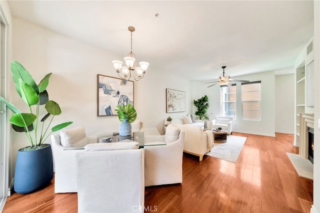 living area featuring a chandelier, light wood-type flooring, a lit fireplace, a ceiling fan, and baseboards