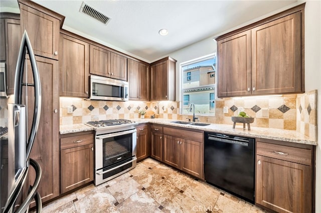 kitchen with appliances with stainless steel finishes, a sink, light stone countertops, backsplash, and recessed lighting