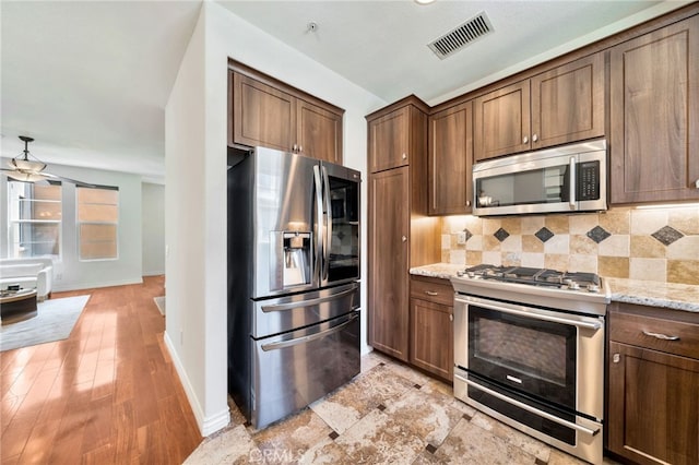 kitchen with appliances with stainless steel finishes, backsplash, baseboards, light stone countertops, and light wood finished floors