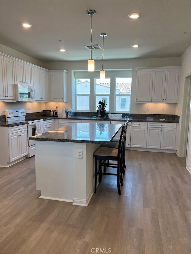 kitchen featuring white appliances, wood finished floors, white cabinets, a center island, and recessed lighting